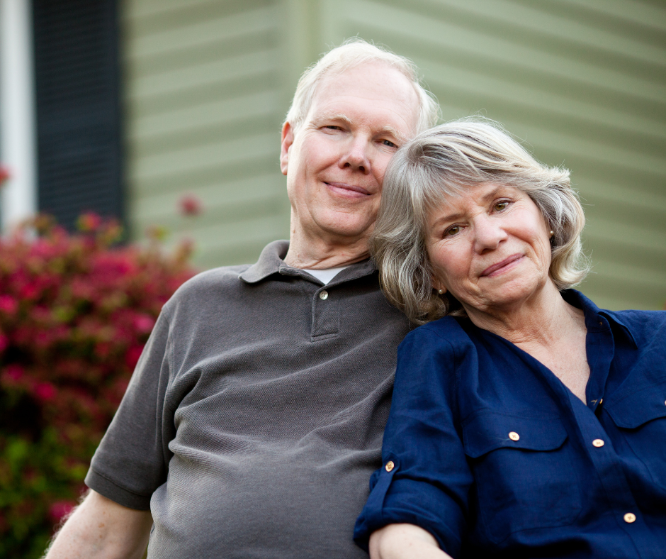 Older couple smiles while sitting in front of their house. 